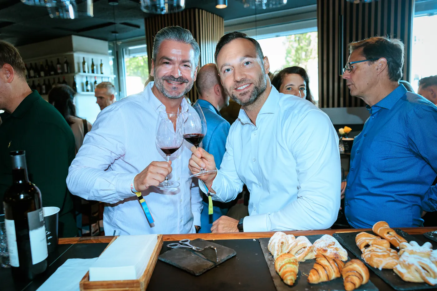 Zwei Gäste stoßen mit Rotwein vor frischen Croissants an