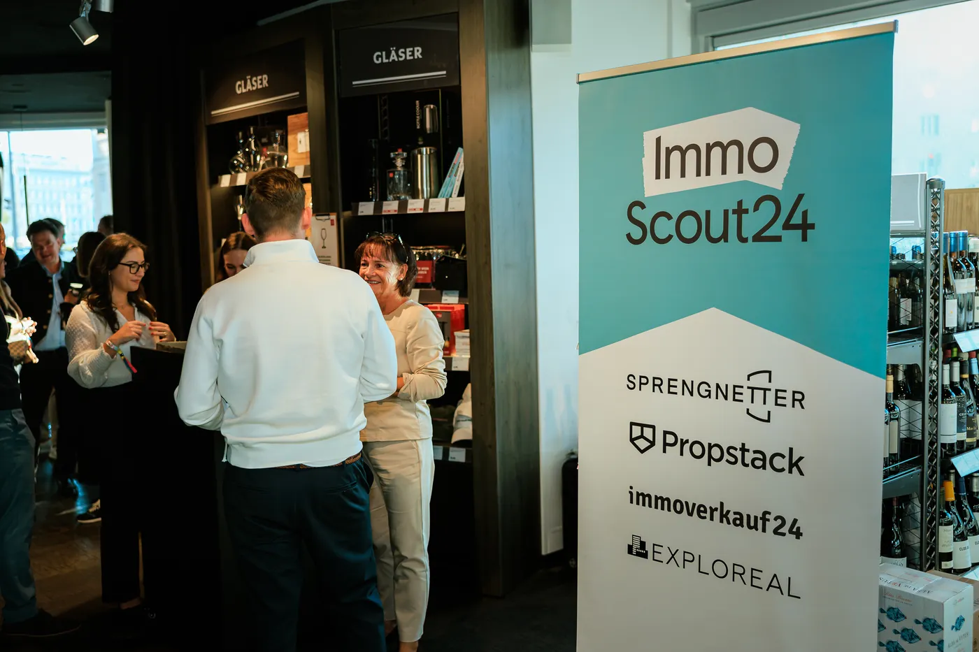 ImmoScout24-Rollup mit Partnerlogos neben dem Gläserregal